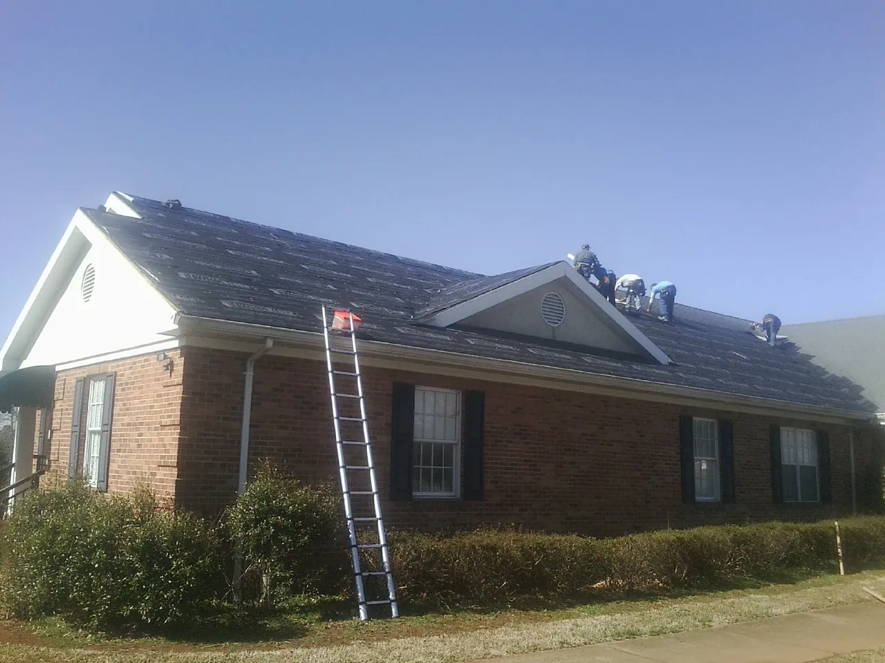 Crew tearing shingles off a brick ranch roof with a ladder set — Emergency Roof Repair work by our crew in Northport