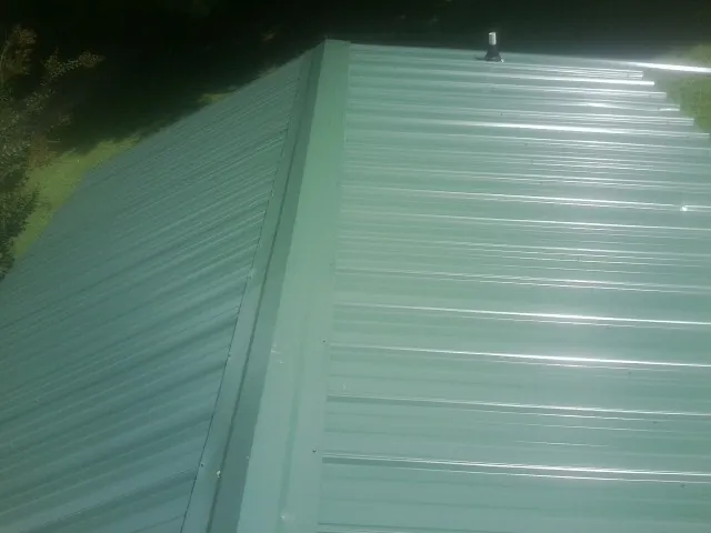 New green metal panels meeting at the ridge of a roof — Flat Roof Repair work by our crew in Northport