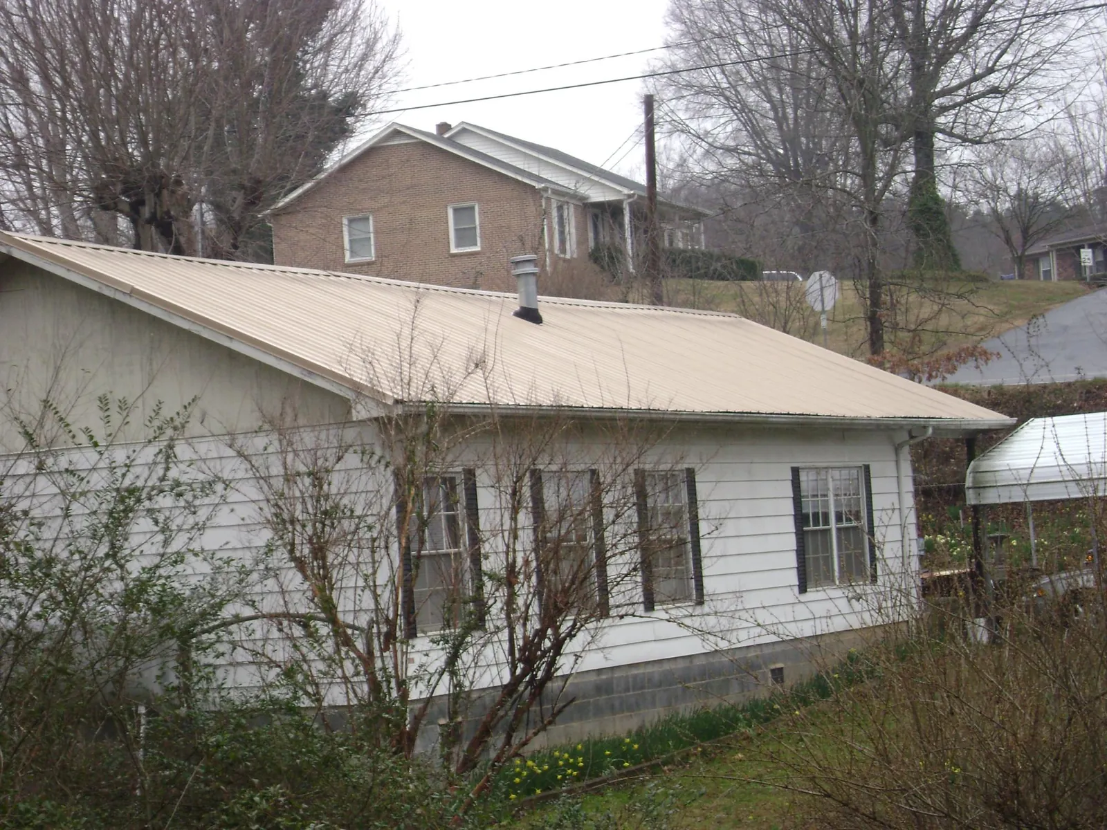 Tan metal roof on a white sided house set into a hillside — Commercial Roofing by Roofing Brothers in Northport