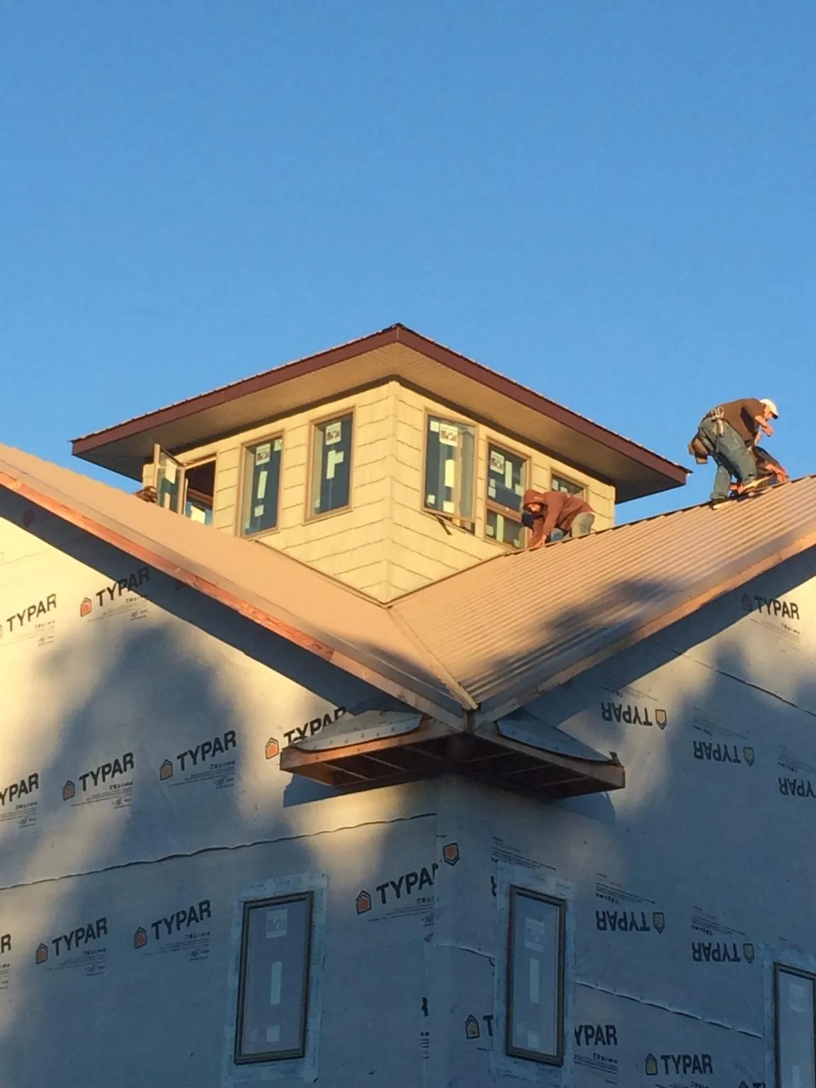 Roofers working around a rooftop cupola on a new metal roof at sunset — Roof Waterproofing in Northport by Roofing Brothers